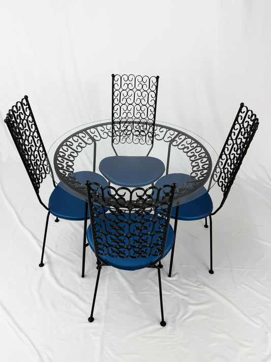 Wrought Iron dining set with four blue cushioned chairs and a round glass top table on a white background