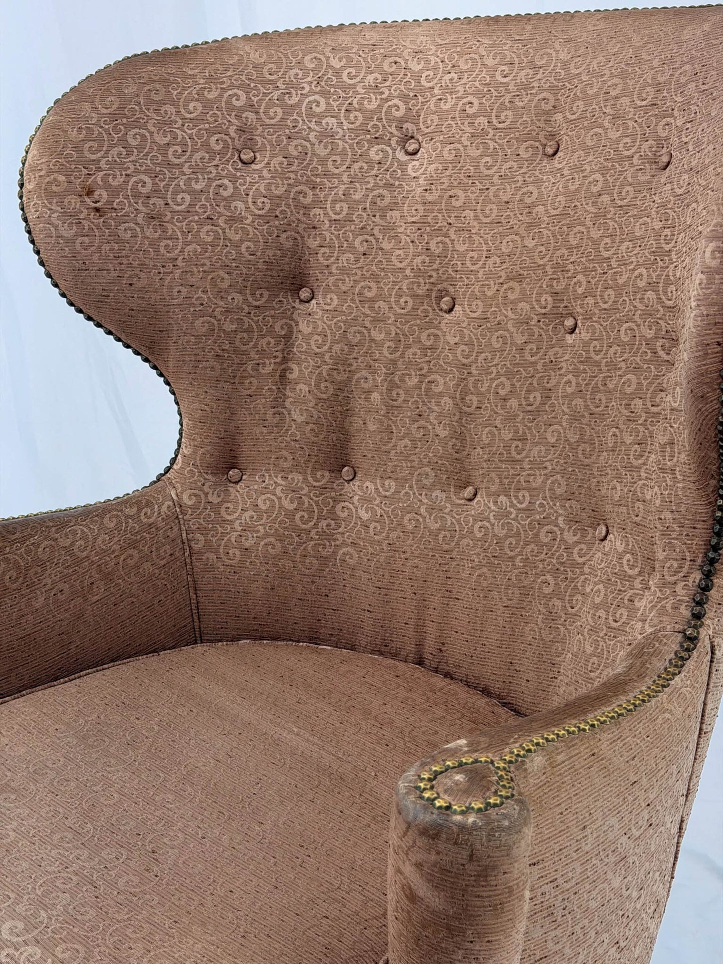 A wingback chair with blush colored upholstery on a white background