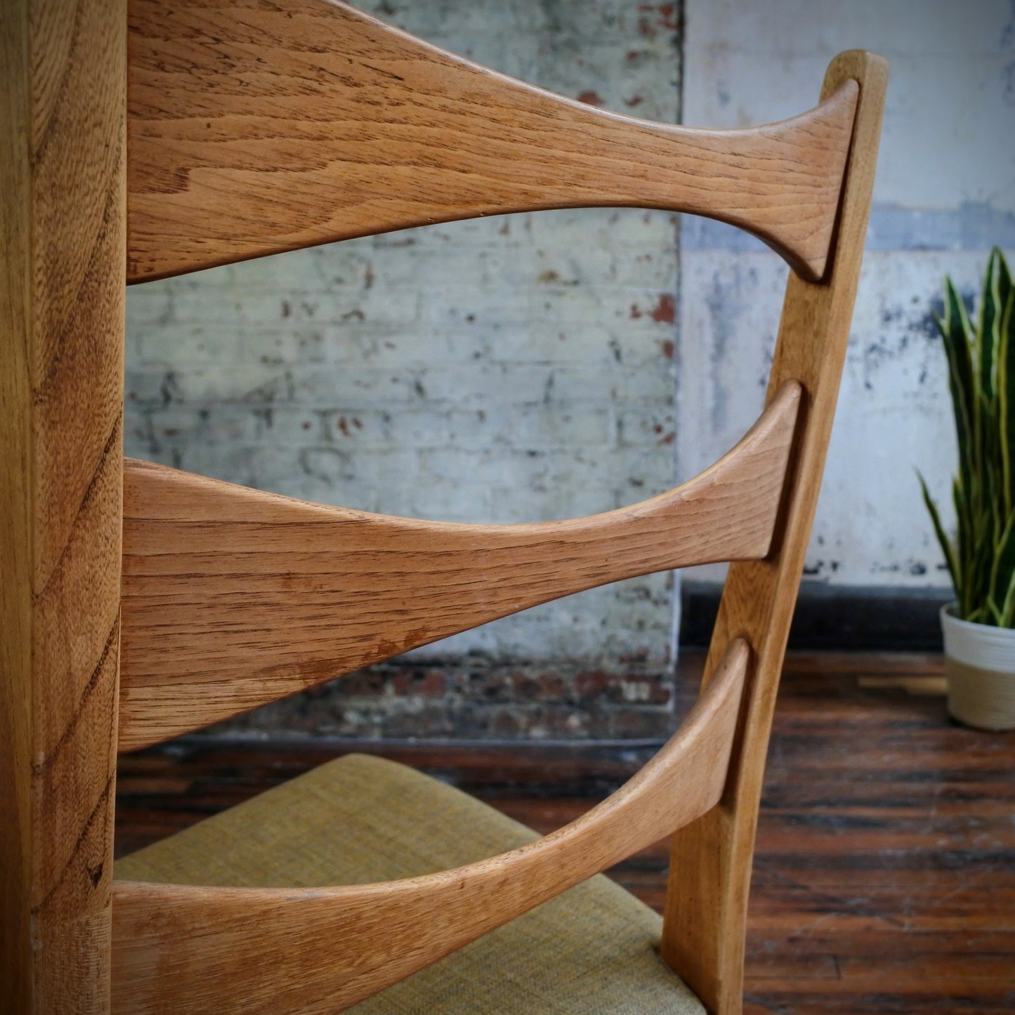 Wooden chair with a beige cushion on a wooden floor against a textured wall.