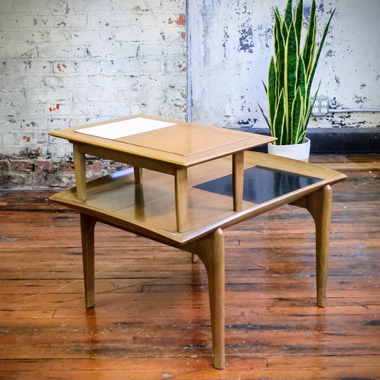 Wooden side table with tile top on a wooden floor with a plant in the background.