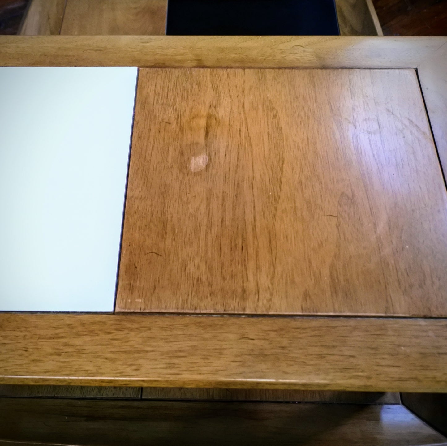 Wooden side table with tile top on a wooden floor with a plant in the background.
