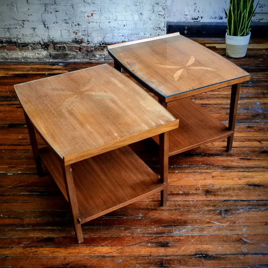 Two wooden side tables on a rustic wooden floor with a plant in the background.