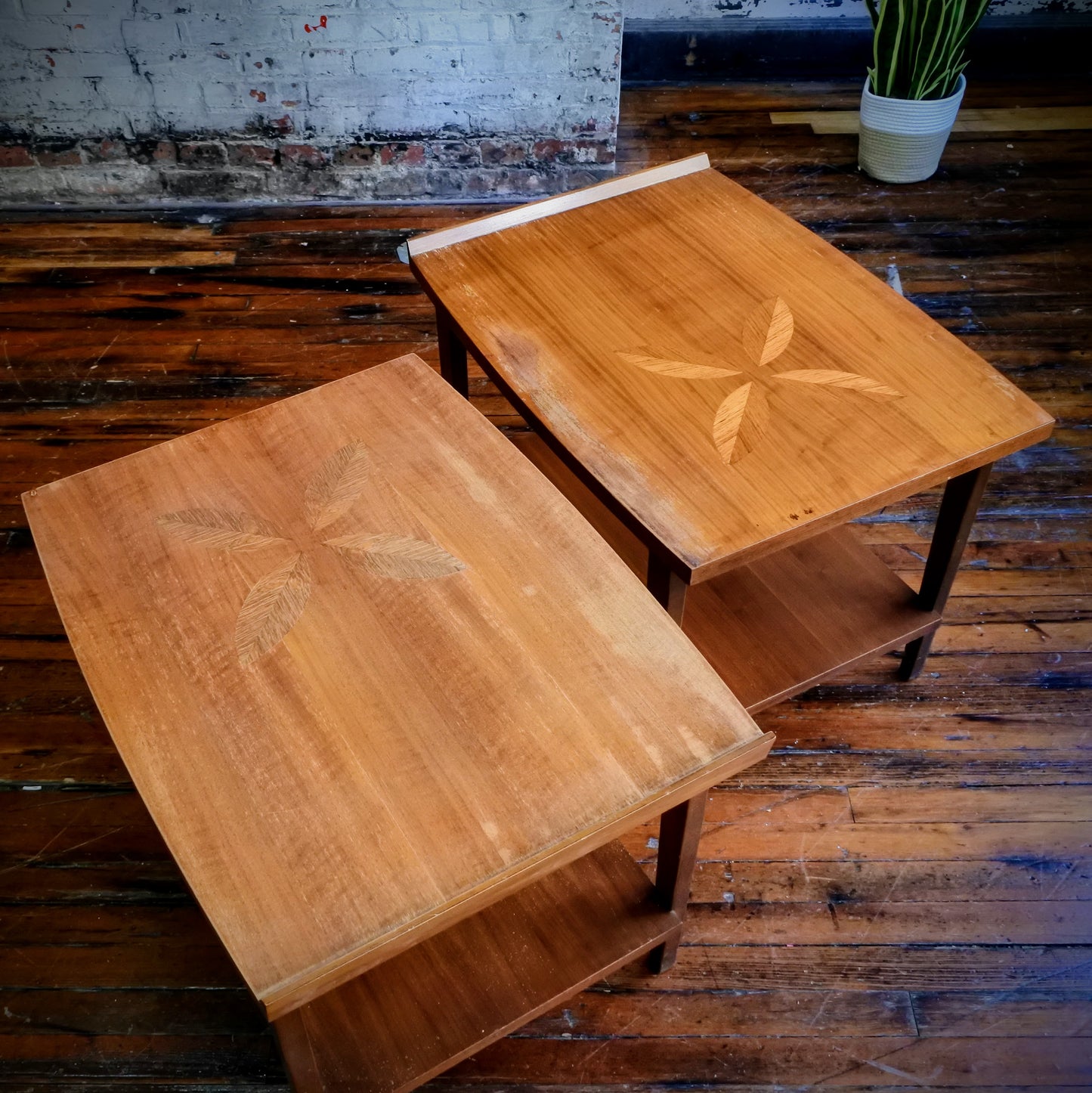 Two wooden side tables on a rustic wooden floor with a plant in the background.