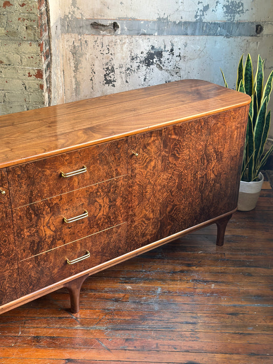 Wooden dresser with a textured finish on a wooden floor with a plant in the background.