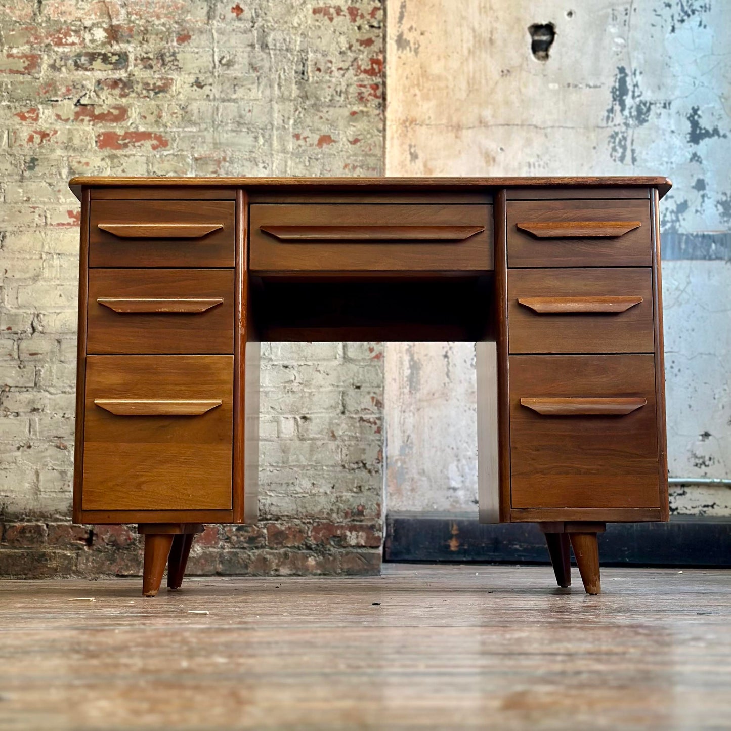 Wooden desk with multiple drawers against a textured wall.