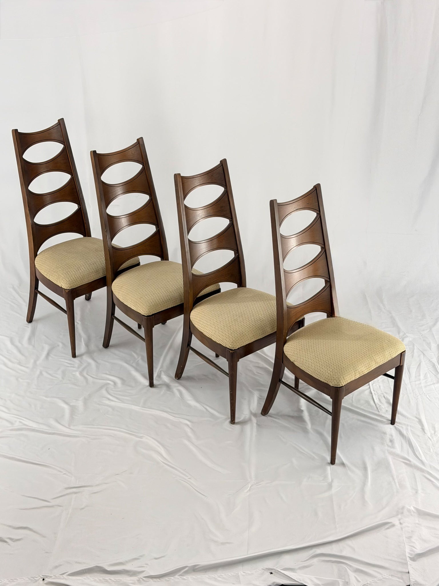 Four wooden chairs with beige cushioned seats on a white background
