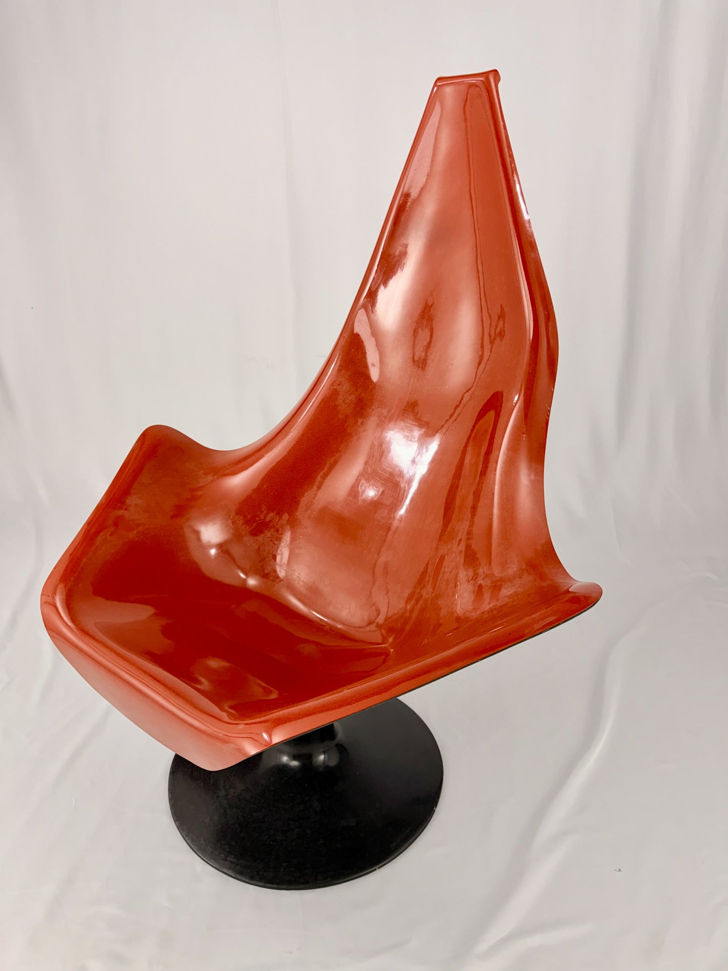 Spage Age fiberglass orange chair with a black base on a white background