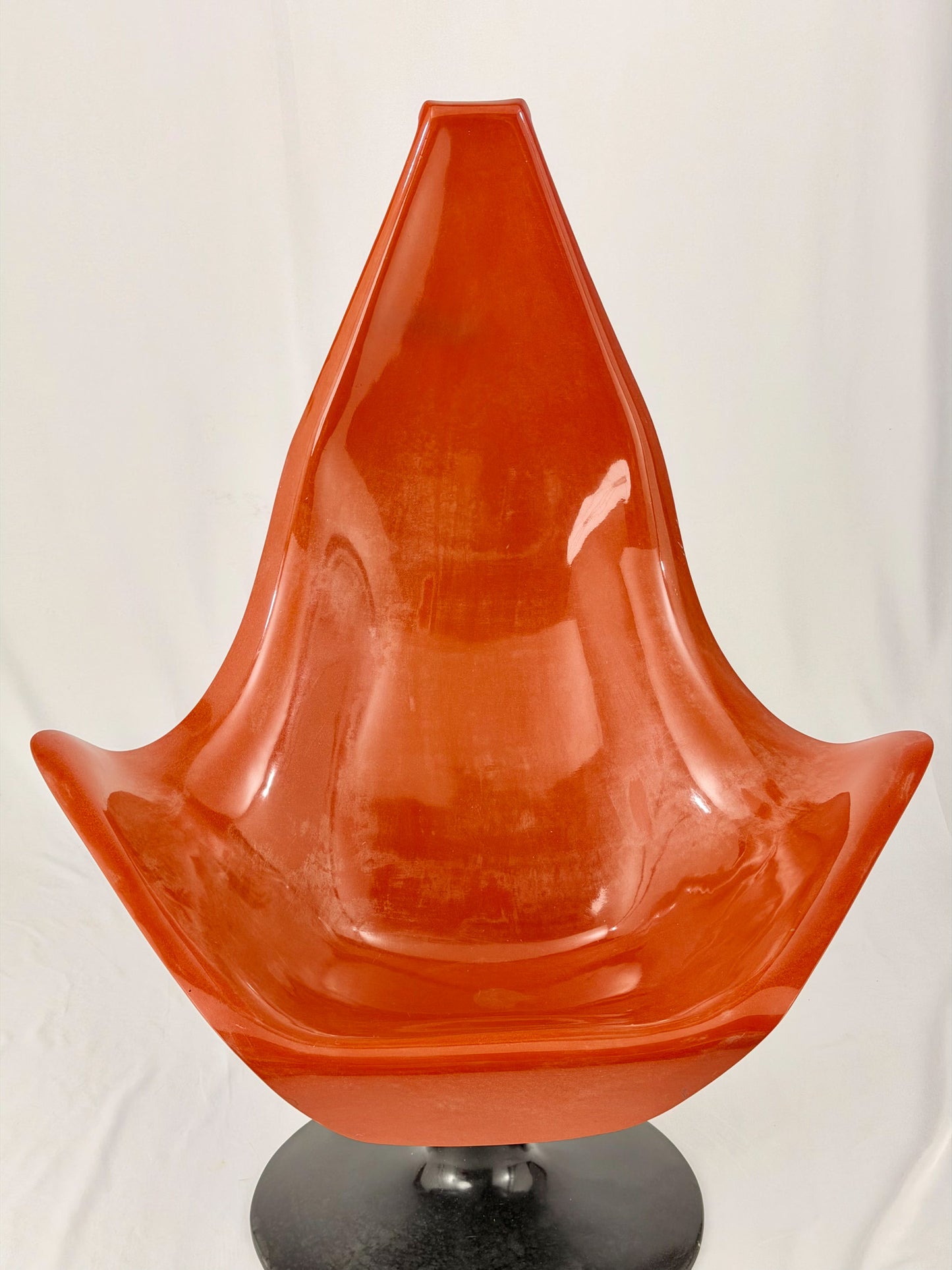 Spage Age fiberglass orange chair with a black base on a white background