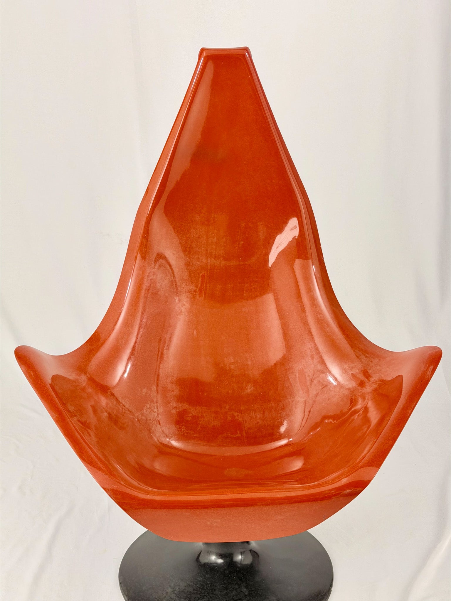 Spage Age fiberglass orange chair with a black base on a white background