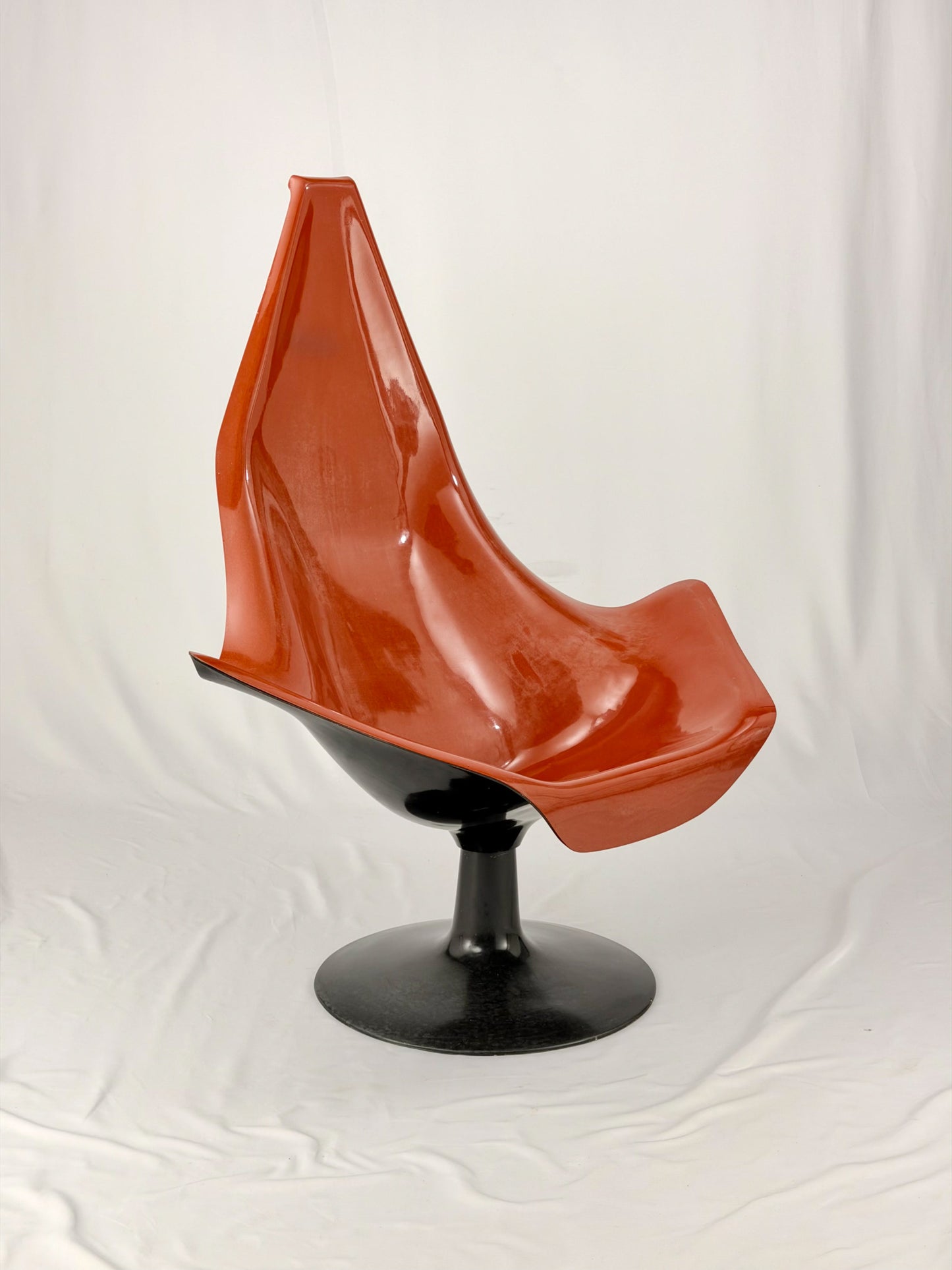 Spage Age fiberglass orange chair with a black base on a white background