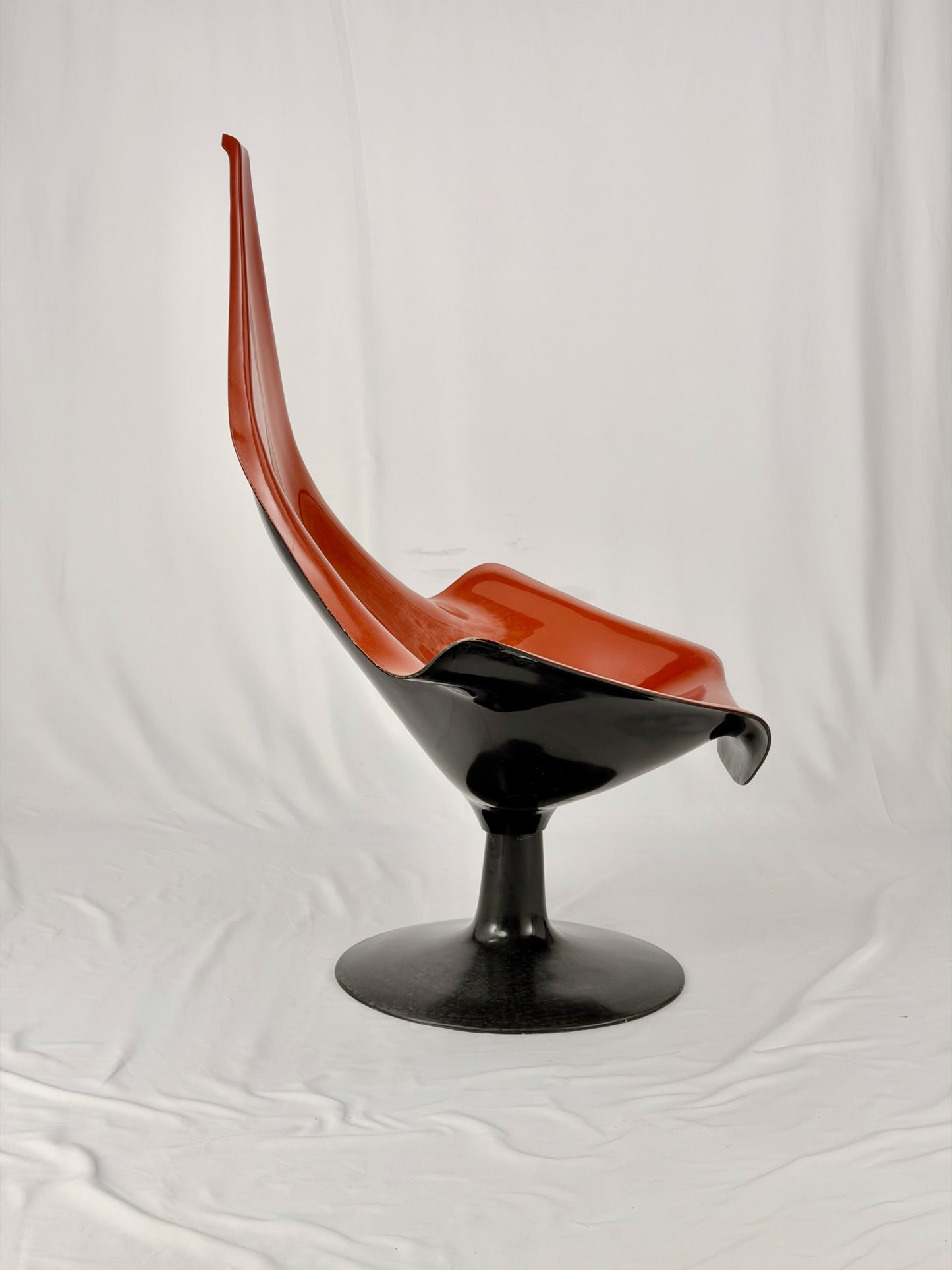 Spage Age fiberglass orange chair with a black base on a white background