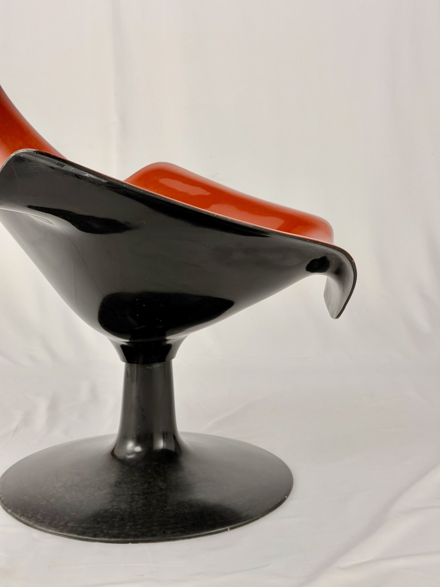 Spage Age fiberglass orange chair with a black base on a white background