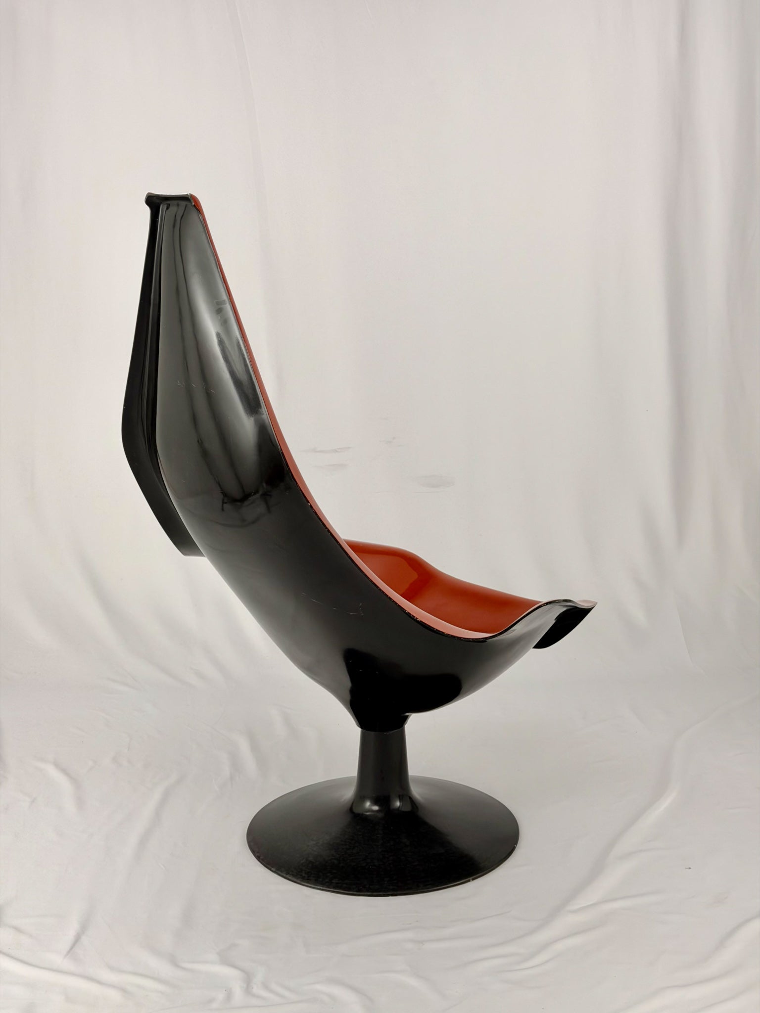 Spage Age fiberglass orange chair with a black base on a white background