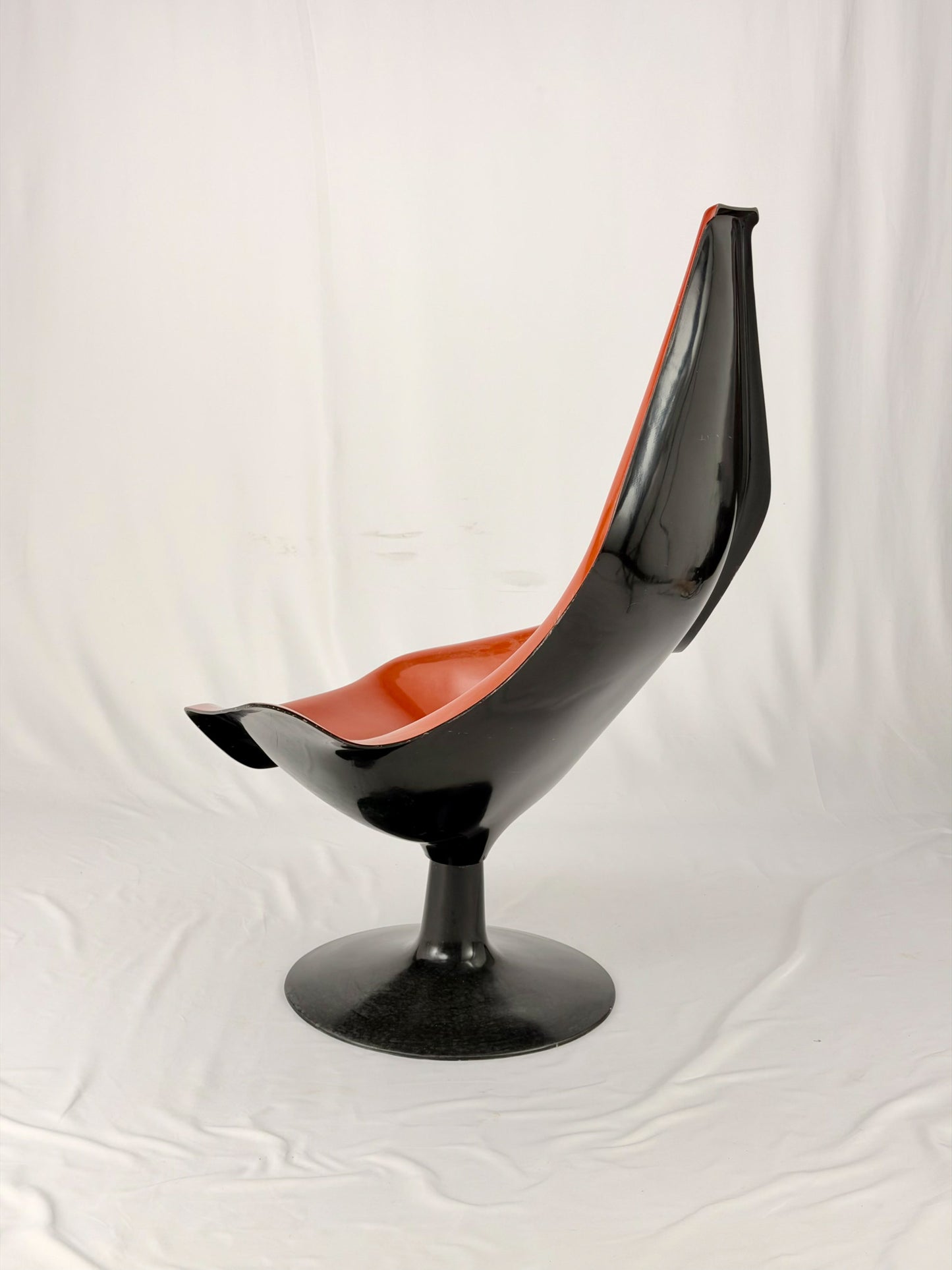 Spage Age fiberglass orange chair with a black base on a white background