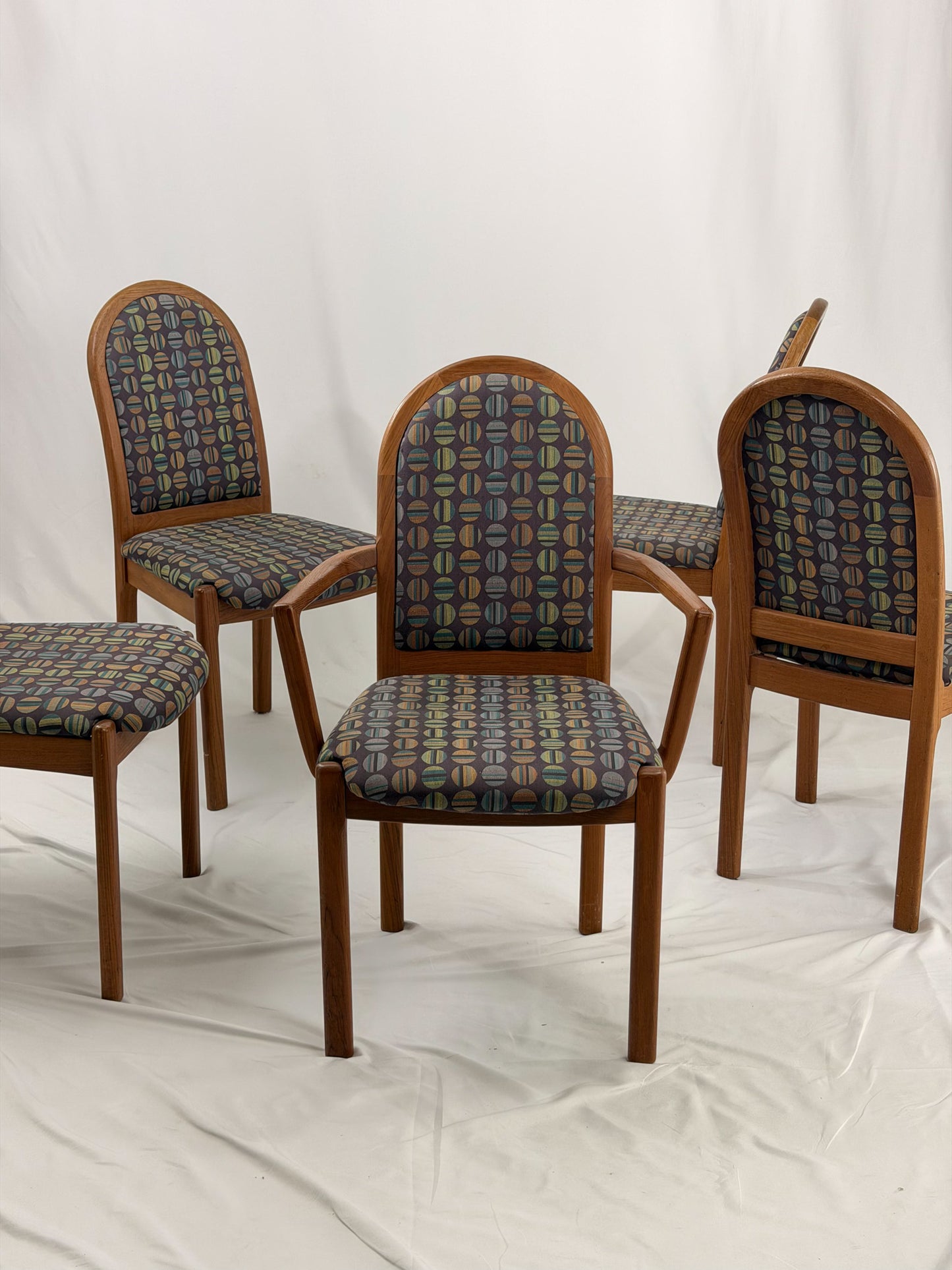 Five wooden chairs with patterned cushion seats on a white background