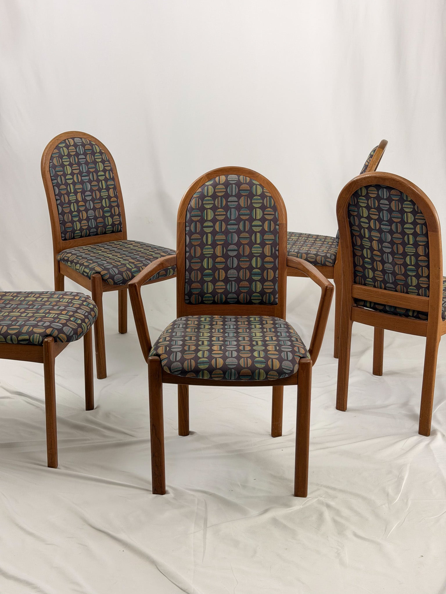 Five wooden chairs with patterned cushion seats on a white background