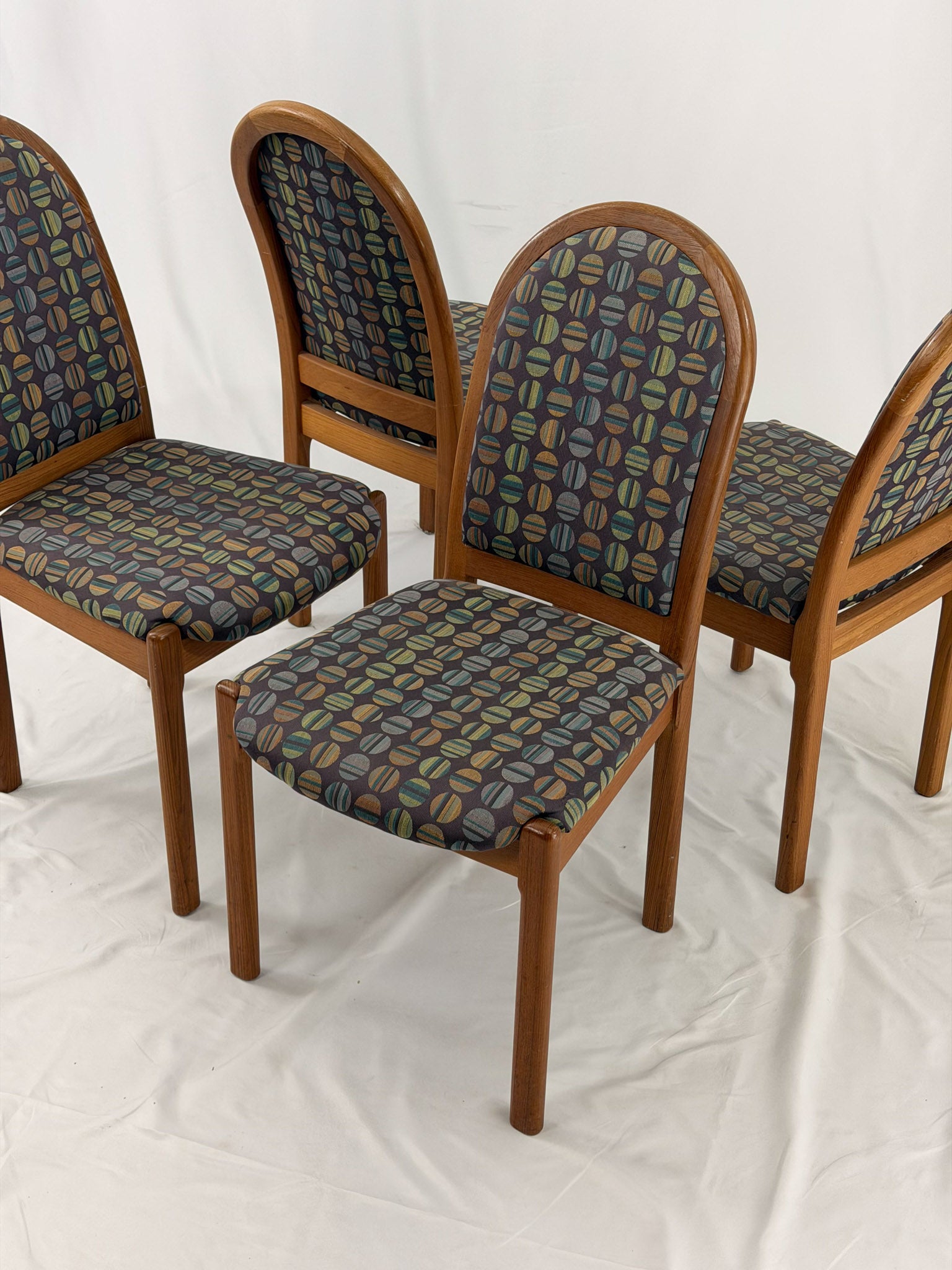 Four wooden chairs with patterned fabric seats on a white background