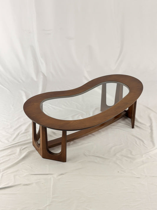 Wooden kidney shaped coffee table with a glass top on a white background
