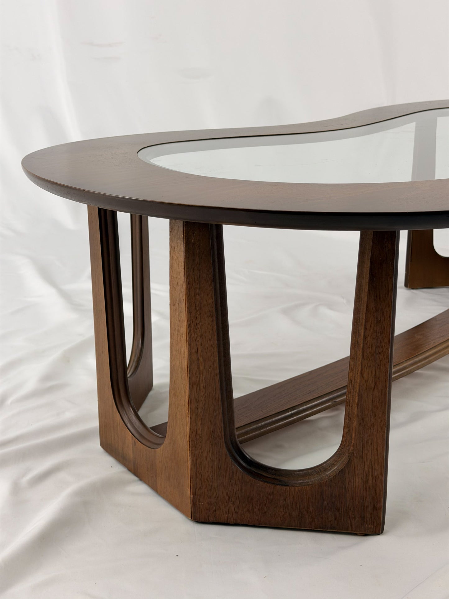 Wooden kidney shaped coffee table with a glass top on a white background