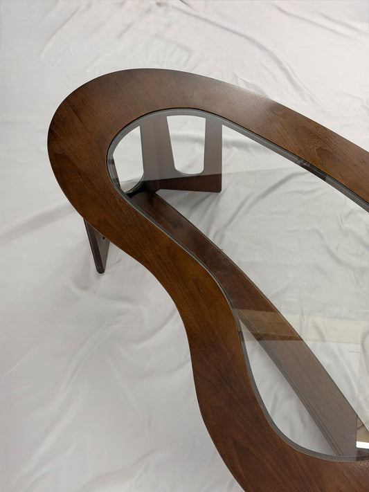 Wooden kidney shaped coffee table with a glass top on a white background