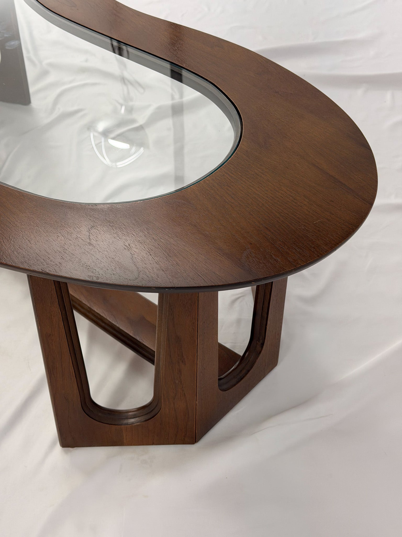 Wooden kidney shaped coffee table with a glass top on a white background