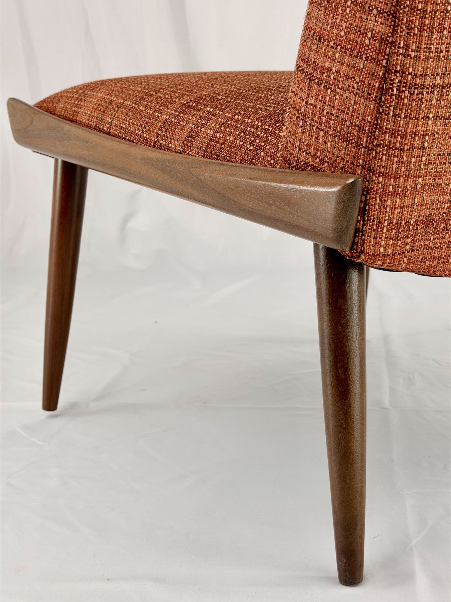 Close-up of a chair with wooden legs and a orange fabric seat on a white background