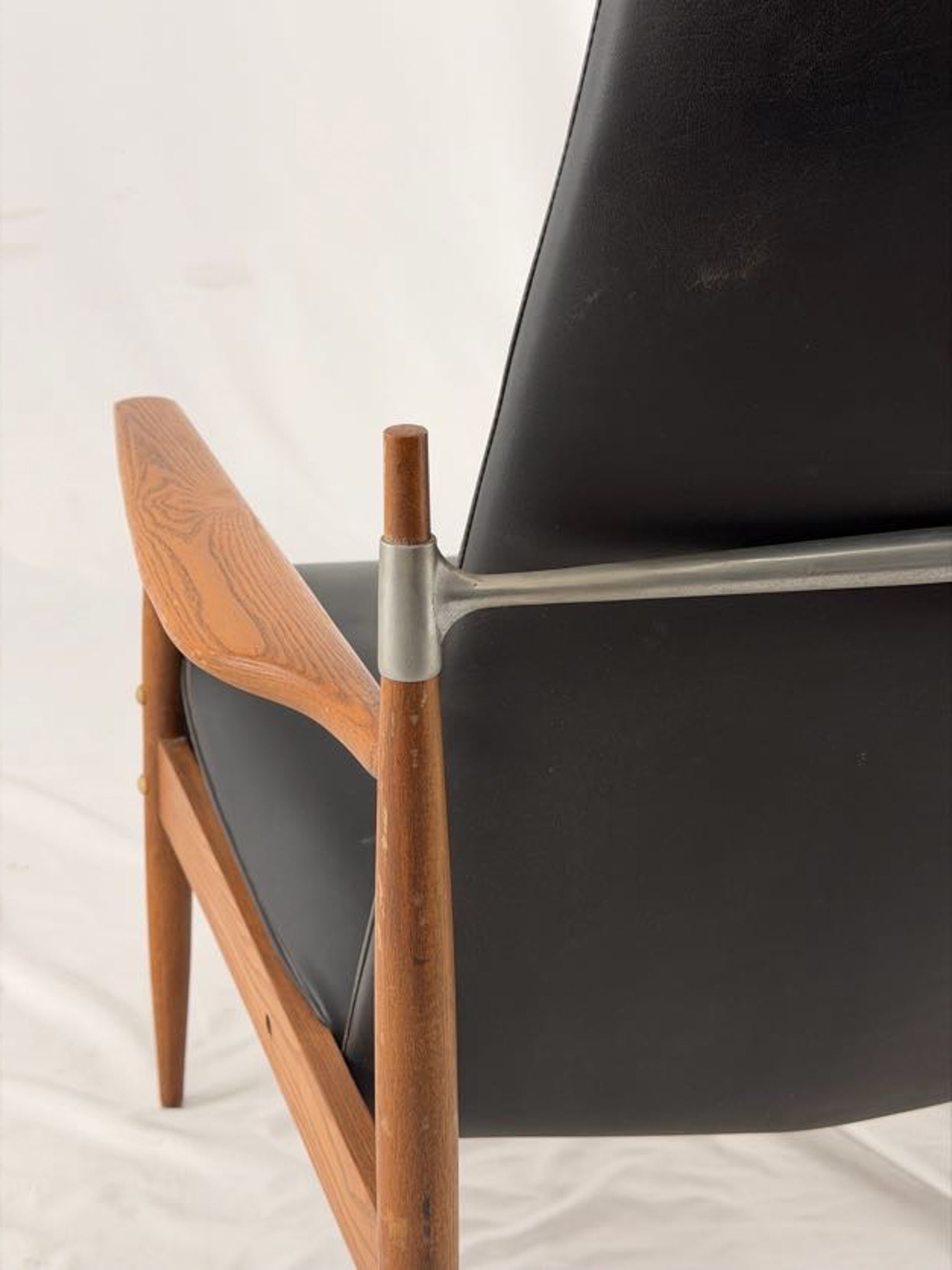 Close-up of a modern chair with wooden frame and black cushion on a light background