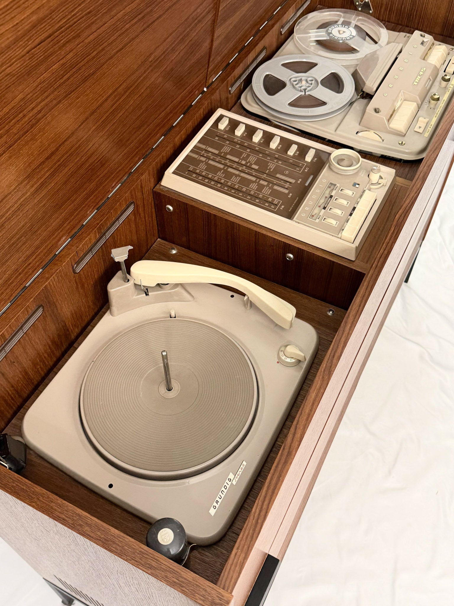 Vintage turntable and reel-to-reel tape recorder inside a wooden cabinet.