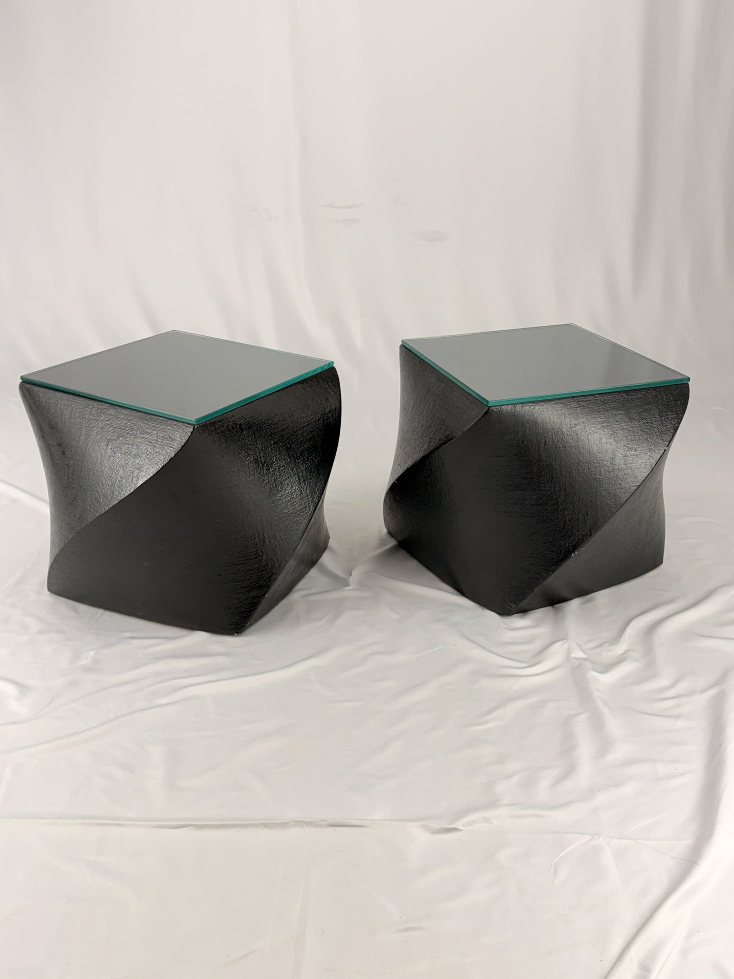 Two geometric black side tables on a white fabric background