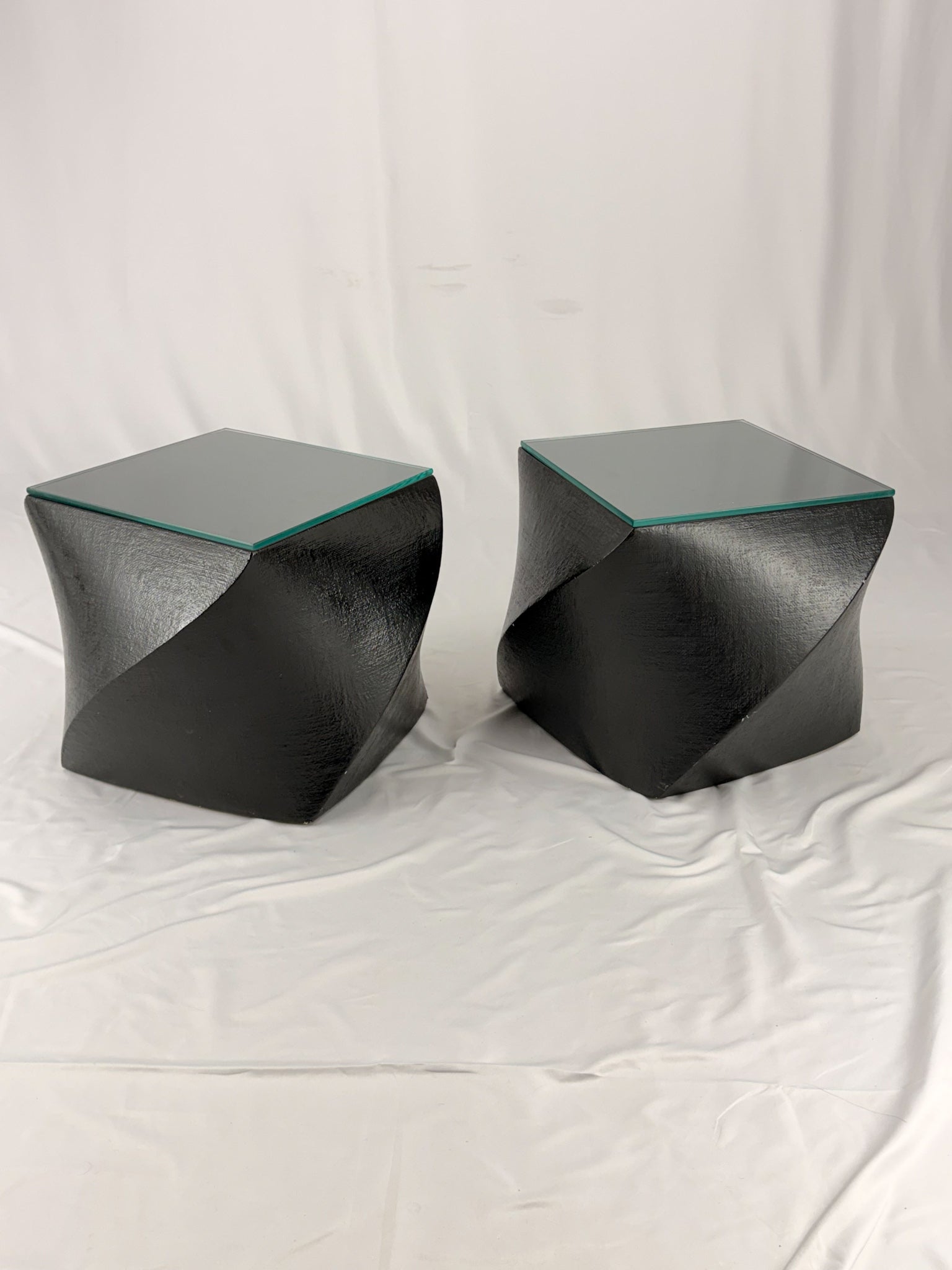 Two geometric black side tables on a white fabric background