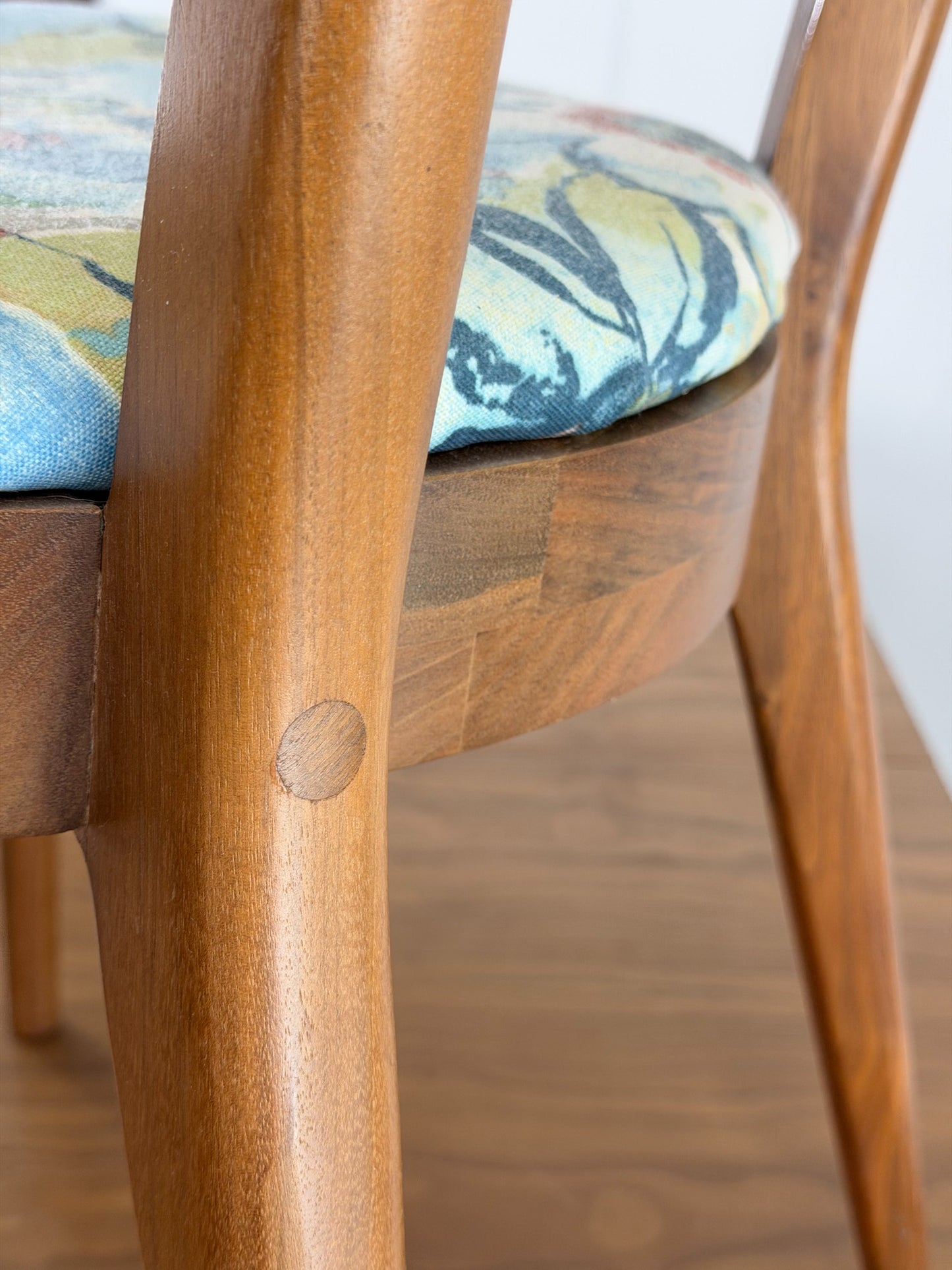 Close-up of a wooden chair with a floral cushion on a wooden floor.