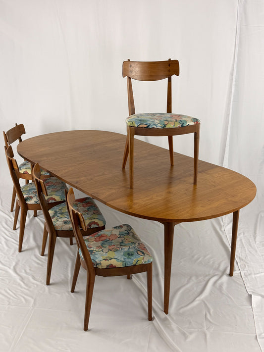 Wooden dining table with fivematching chairs featuring floral cushions on a white background