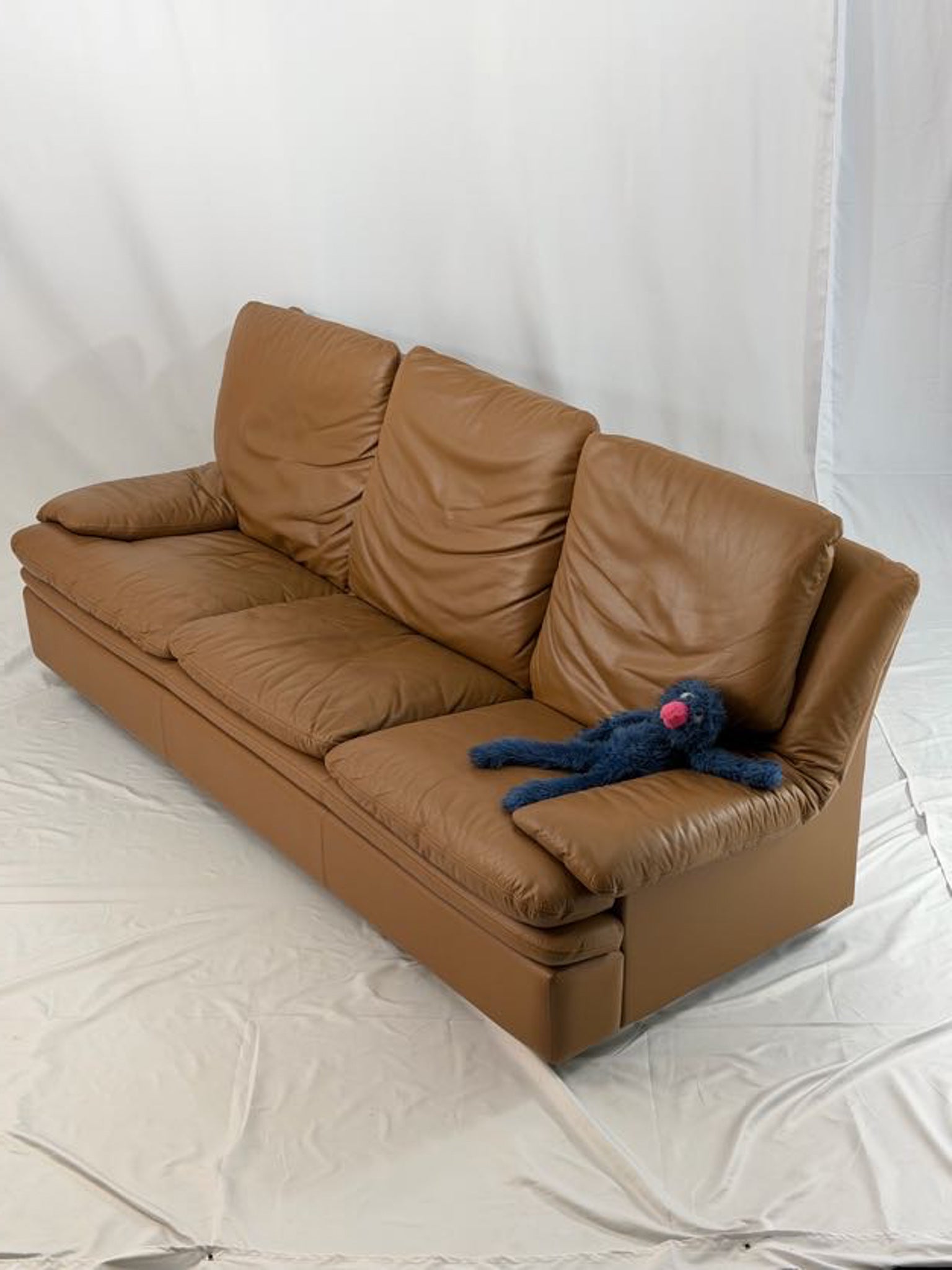 Brown leather sofa with a blue plush toy on a white background