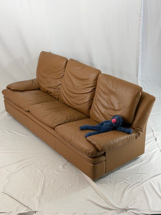 Brown leather sofa with a blue plush toy on a white background