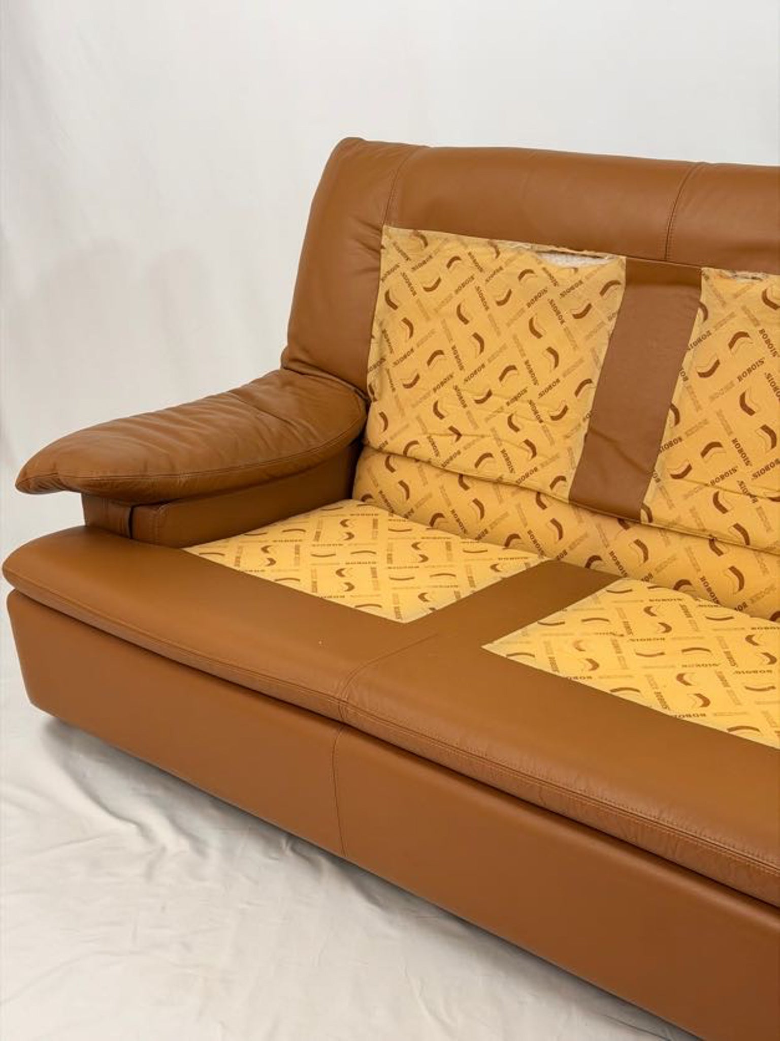 Brown leather sofa with yellow patterned cushions on a white background
