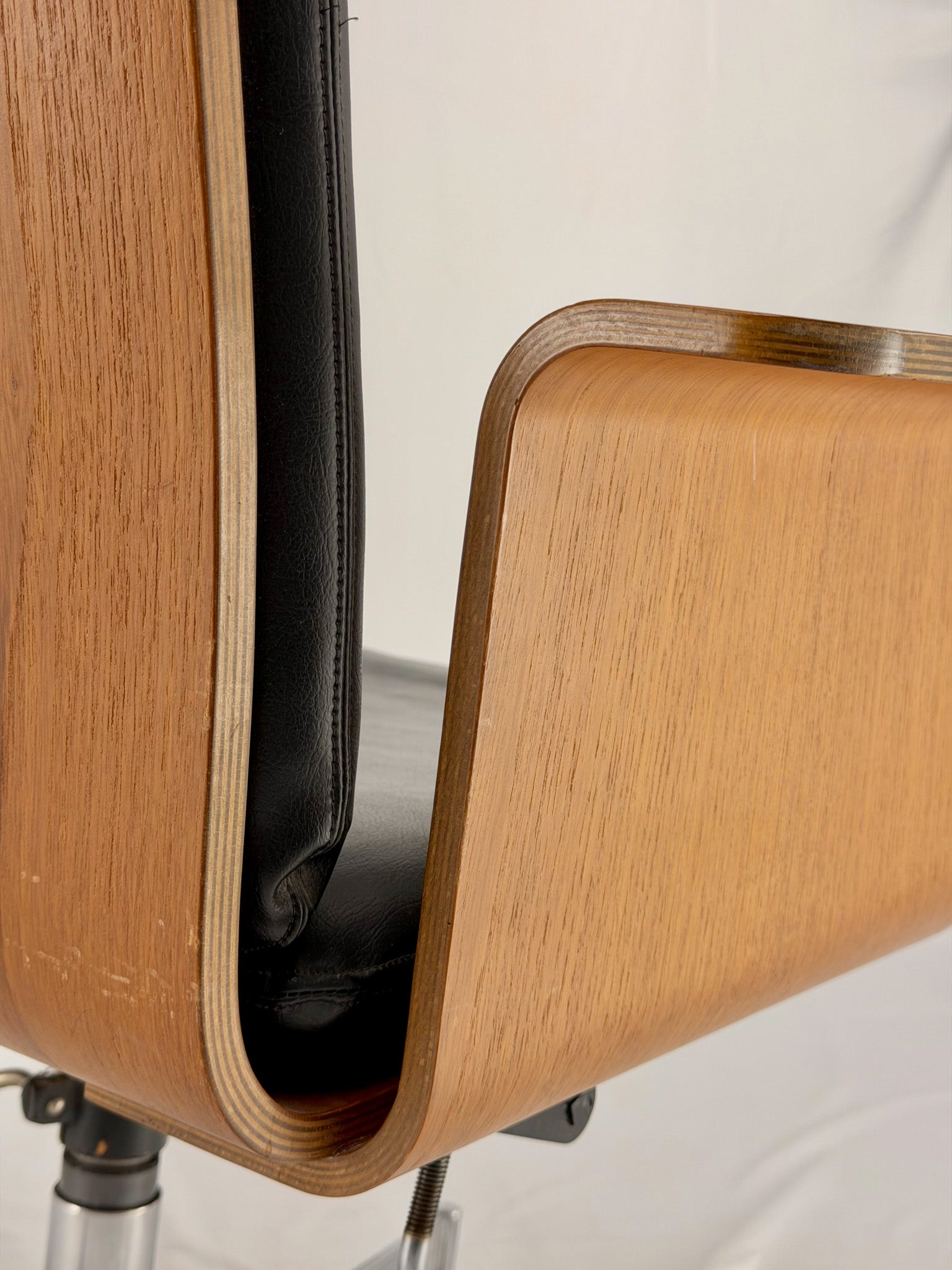 Close-up of a wooden chair with a black seat pad on a light background