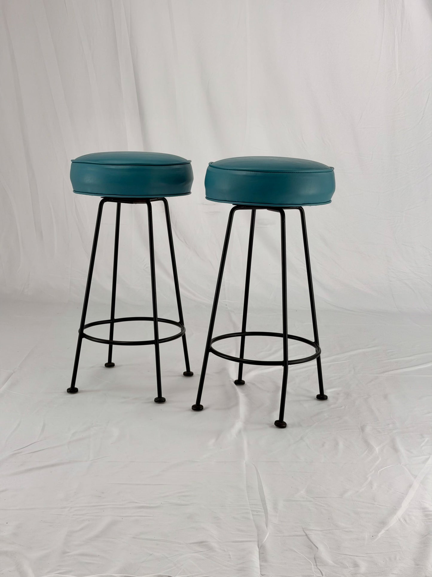 Two teal bar stools with black metal legs on a white background