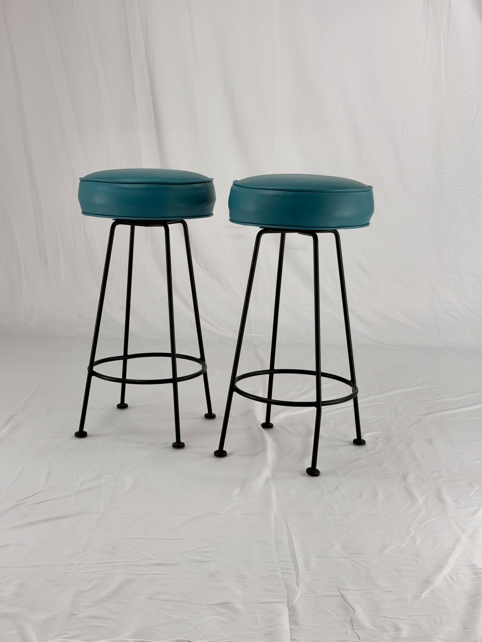 Two teal bar stools with black metal legs on a white background