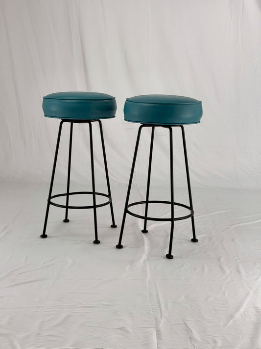 Two teal bar stools with black metal legs on a white background