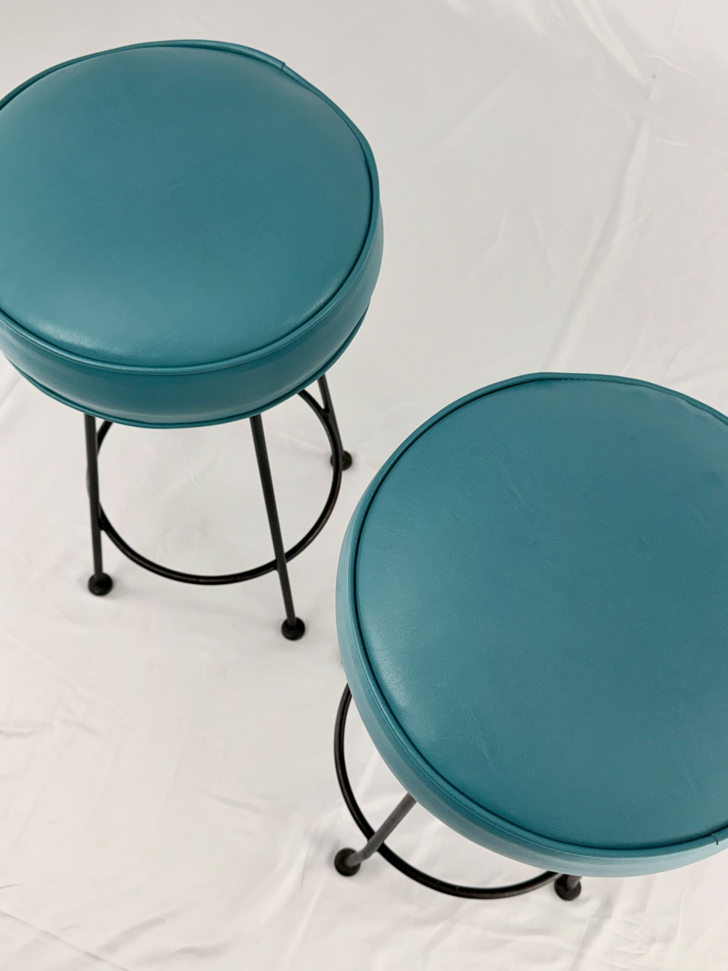 Two teal bar stools with black metal legs on a white background