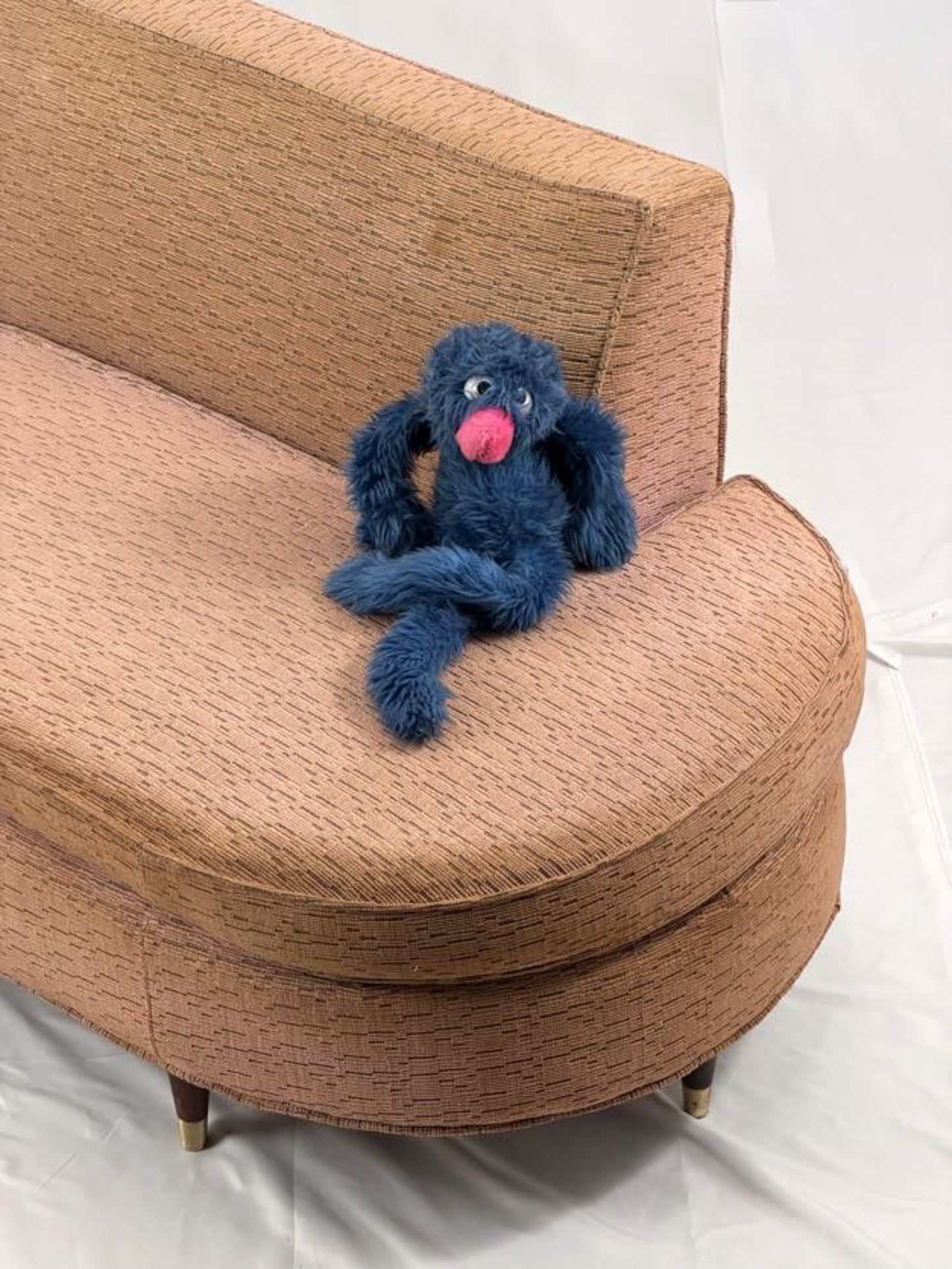 Blue plush toy with a pink nose on a pink couch.