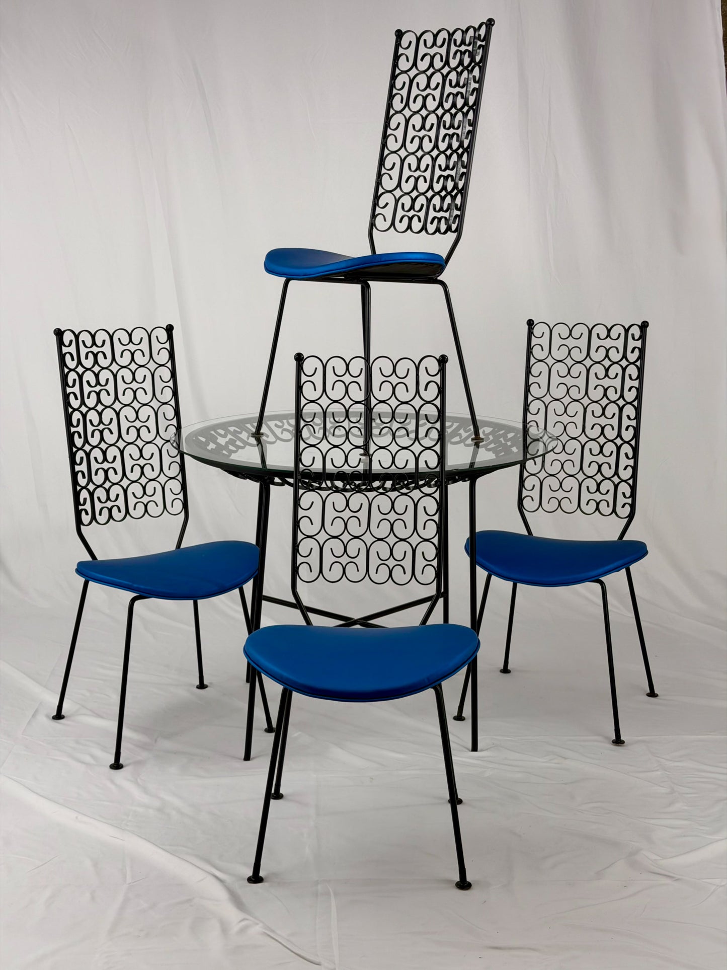 Wrought Iron dining set with four blue cushioned chairs and a round glass top table on a white background