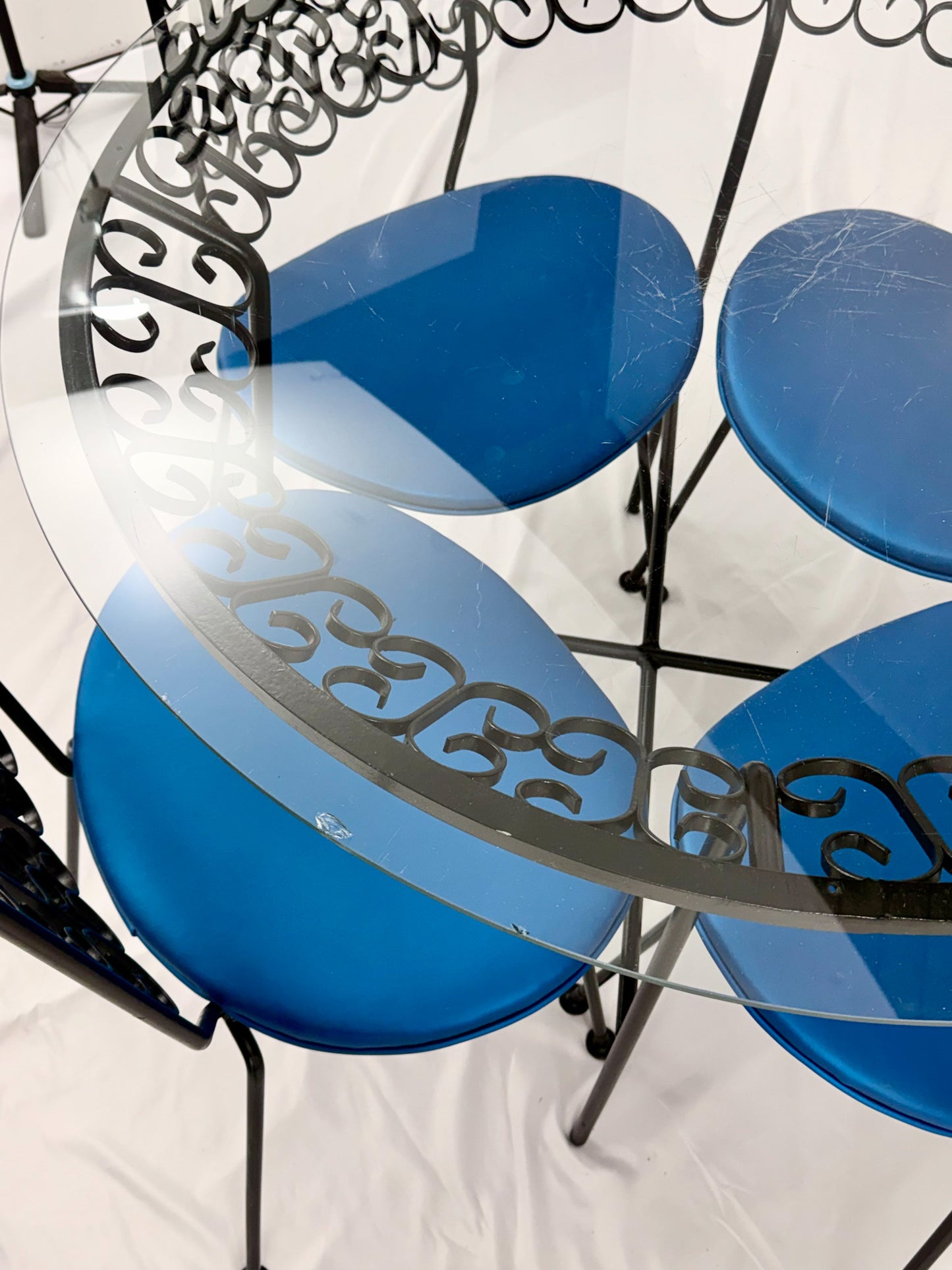 Wrought Iron dining set with four blue cushioned chairs and a round glass top table on a white background