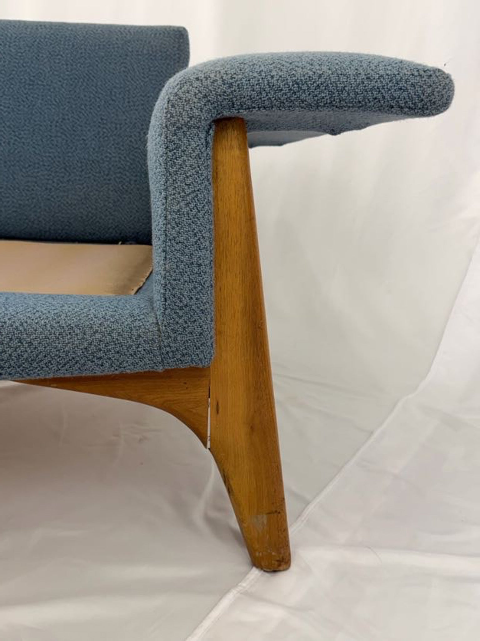 Blue upholstered couch with wooden legs on a white background