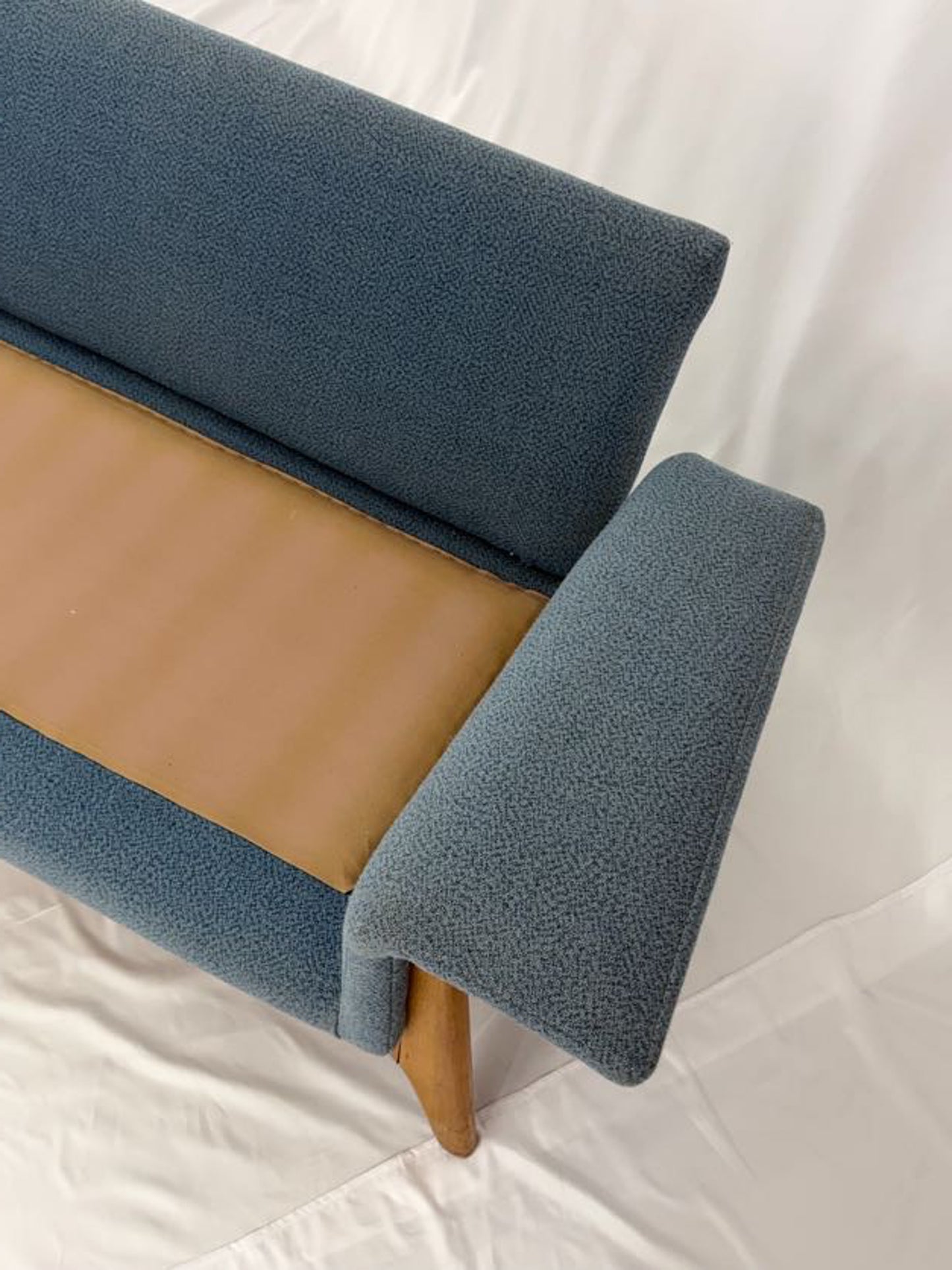Blue upholstered couch with wooden seat on a white background