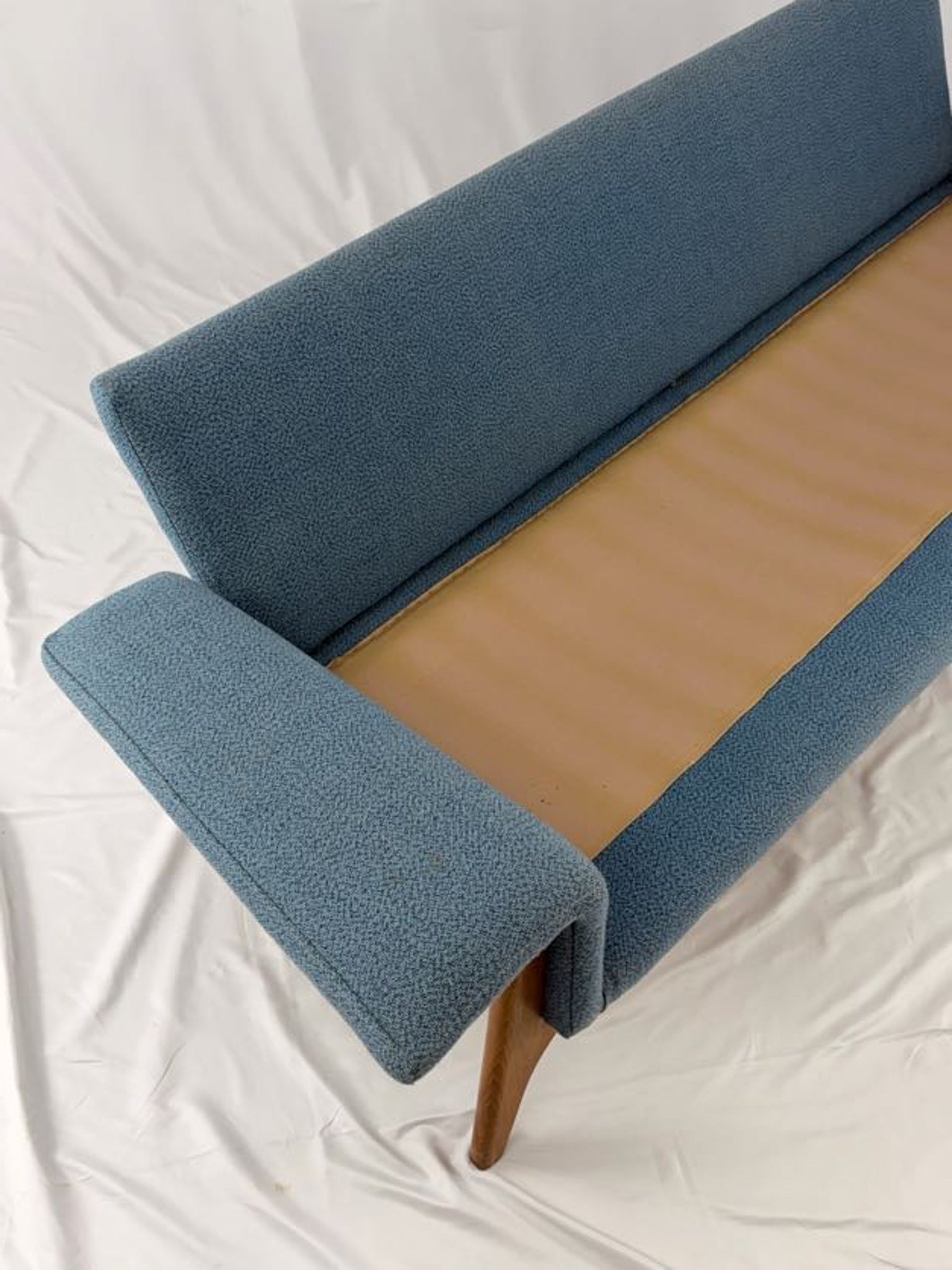 Blue upholstered sofa with wooden legs on a white background