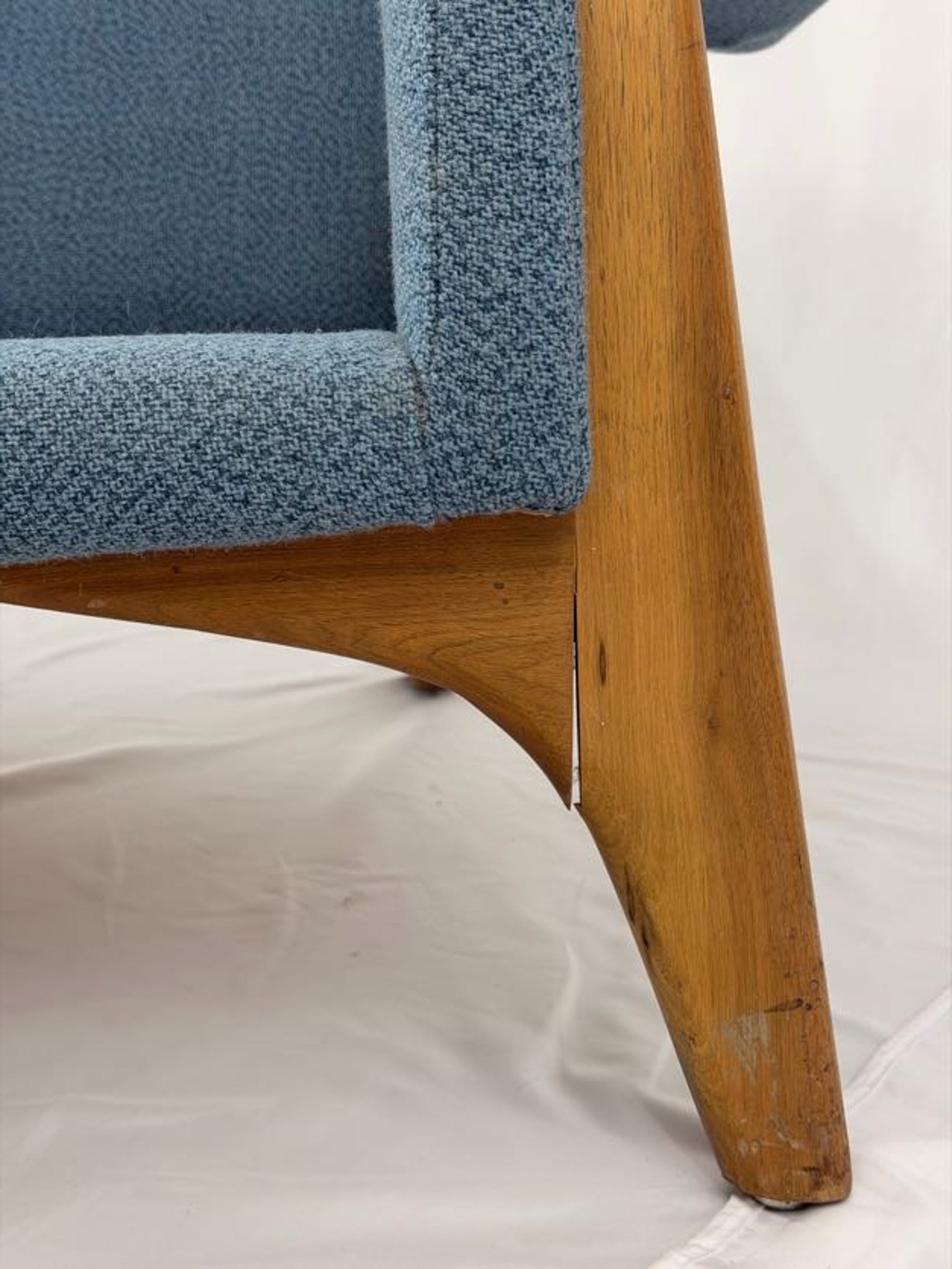 Close-up of a blue upholstered couch with wooden legs on a white background