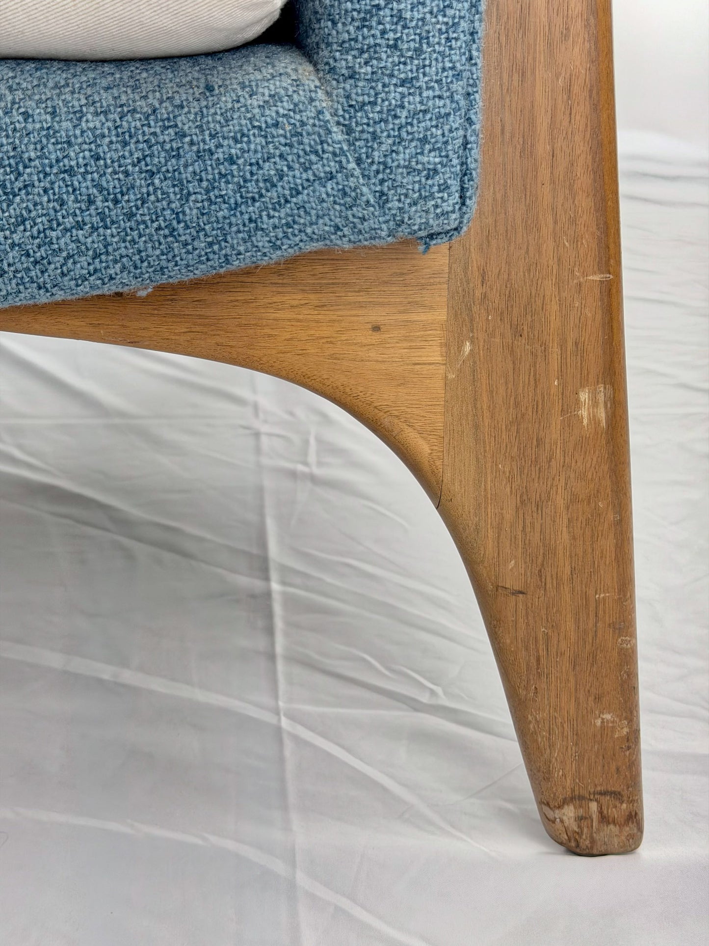 Close-up of a wooden chair leg with a blue cushioned seat on a white background