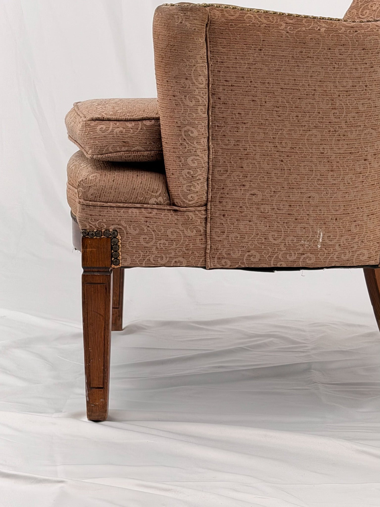 A wingback chair with blush colored upholstery on a white background