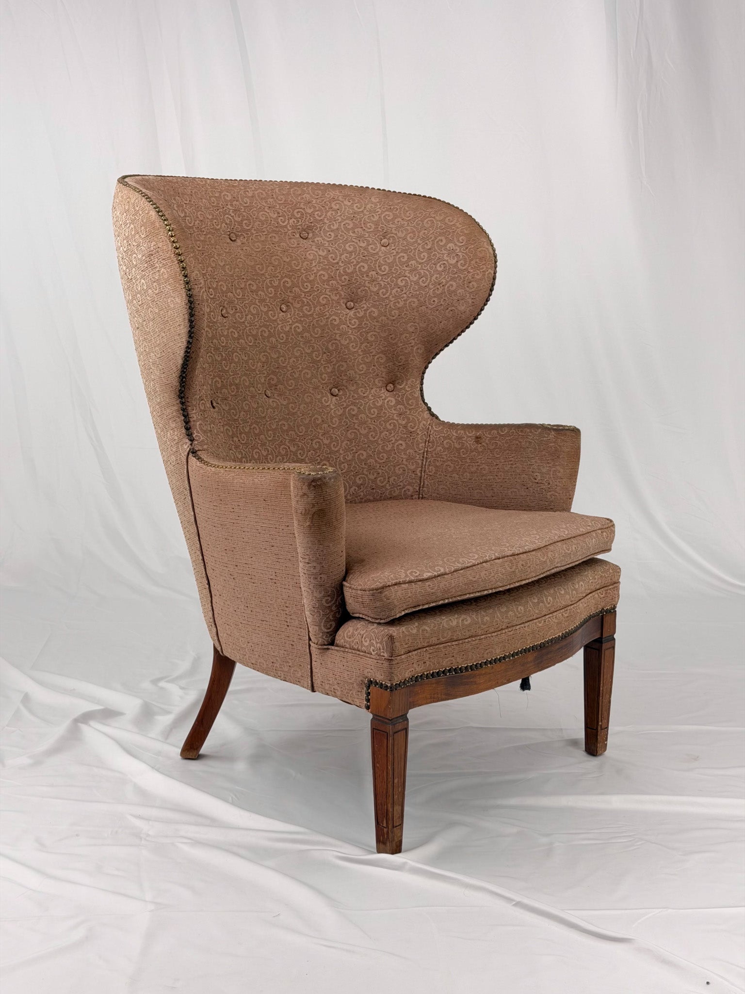 A wingback chair with blush colored upholstery on a white background